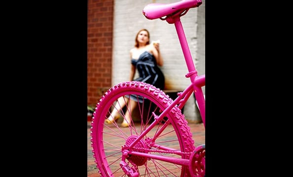 "Pop of Pink" is a shot of a rehabbed bike outside Baked & Wired in Georgetown.  The photographer's roommate, Erin Hamilton—who can be seen in the background— suggested a day of shooting in DC.  To get this winning shot, the photographer had to lie in the