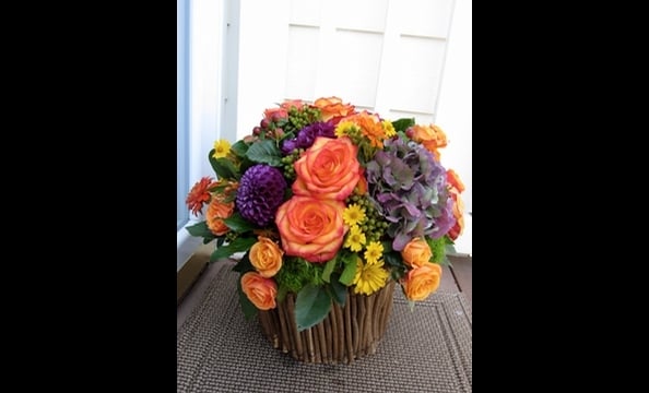 Antique hydrangeas, dahlias, roses, spray roses, berzillia berries, wild daisies, and seasonal foliage in a twig basket.