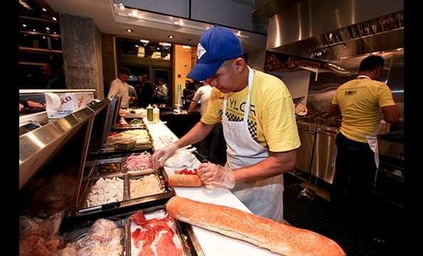 Taylor Gourmet employees whip up sandwiches for the crowd that attended the preview party of the new space.