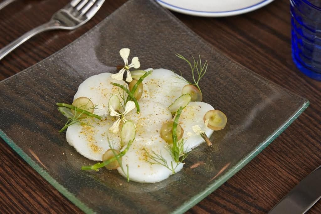 The raw bar includes classics like oysters and shrimp, plus crudo like these sweet scallops with grapes and fennel pollen.