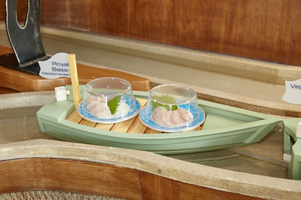 Small dishes like sushi rolls and sashimi float along on boats made by a local woodworker. 