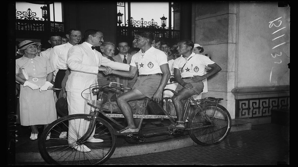 Dr. Loo S. Rowe of Pan-American Union greets Argentinian cyclists Victor Scarraffia (front) and Vincente Gregori (rear) in 1934 after they complete a 2 and a half year journey. 