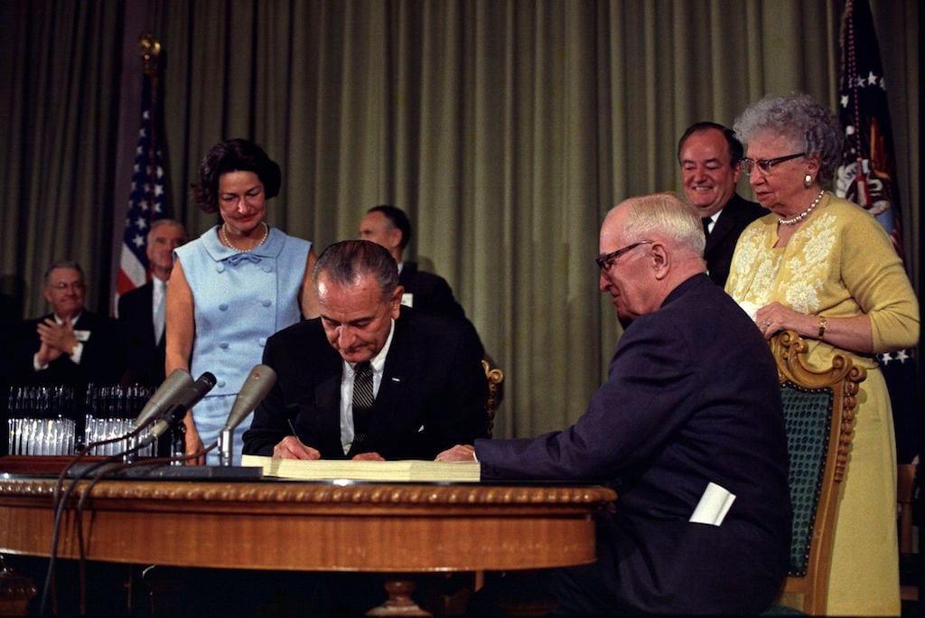President Lyndon B. Johnson (center) signing the Medicare Bill with former President Harry S. Truman (right) at the Harry S. Truman Library in Independence, Missouri. Photo by Executive Office of the President via\wikimediacommons