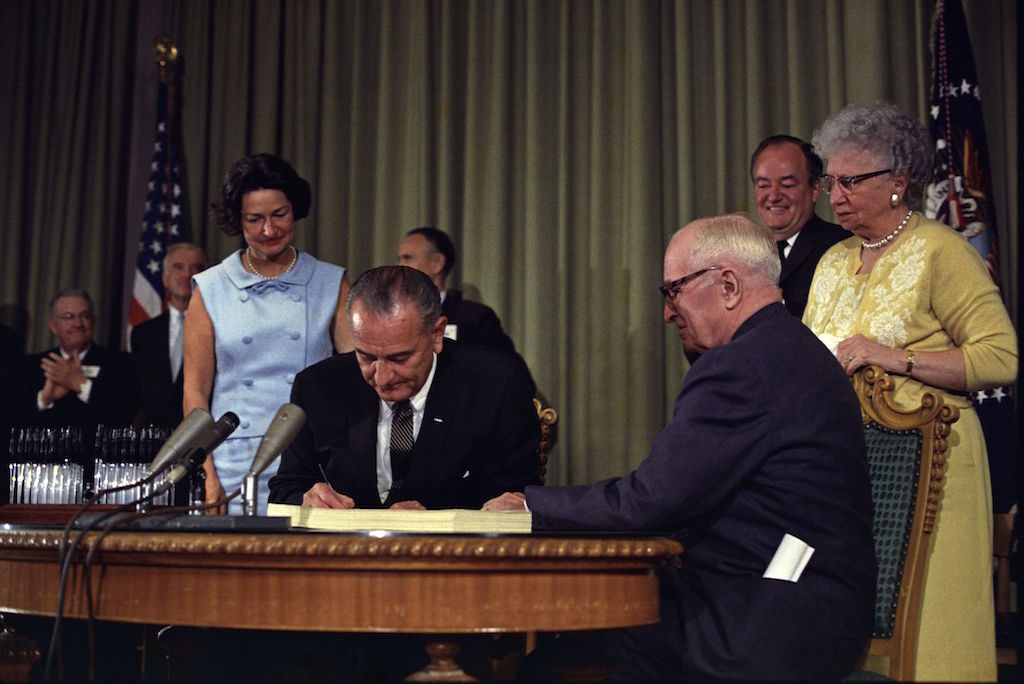 President Lyndon B. Johnson (center) signing the Medicare Bill with former President Harry S. Truman (right) at the Harry S. Truman Library in Independence, Missouri. Photo by Executive Office of the President via\wikimediacommons