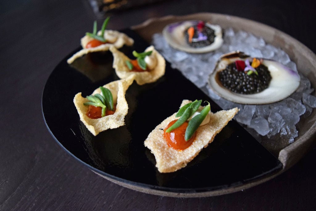 A meal begins with drinks and snacks, like these shrimp chips and sous-vide clams with caviar. 