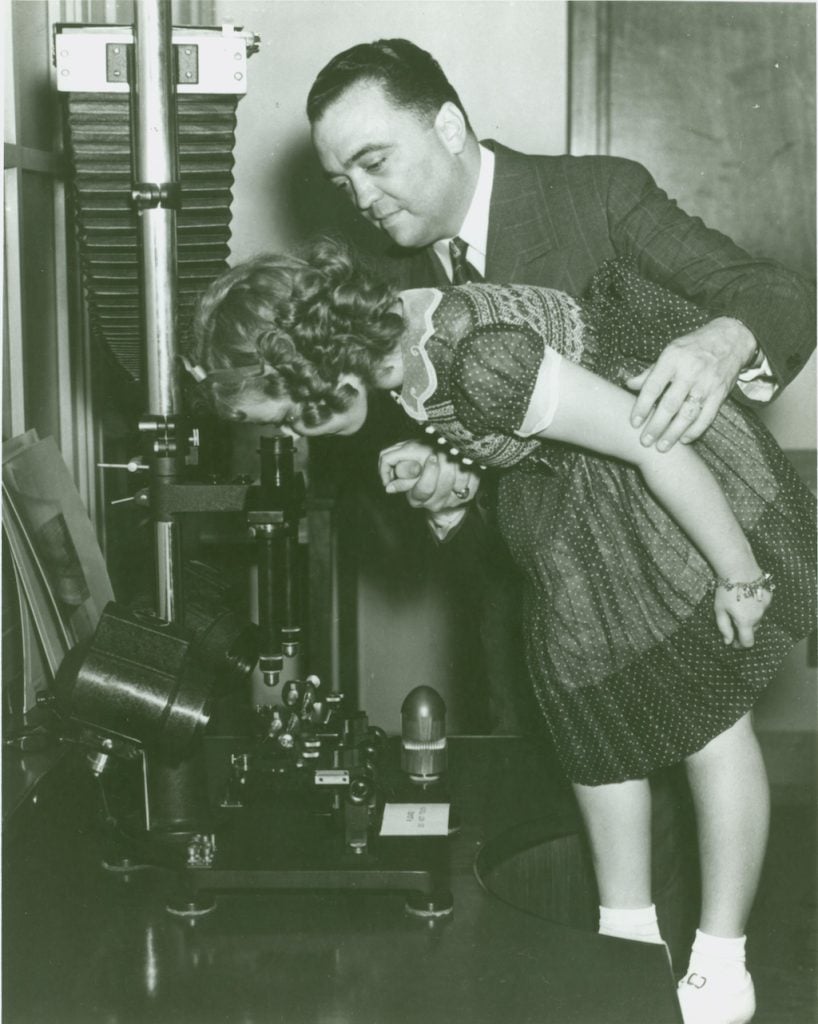 FBI Director J. Edgar Hoover showing actress Shirley Temple a microscope in the FBI's crime lab in 1938.