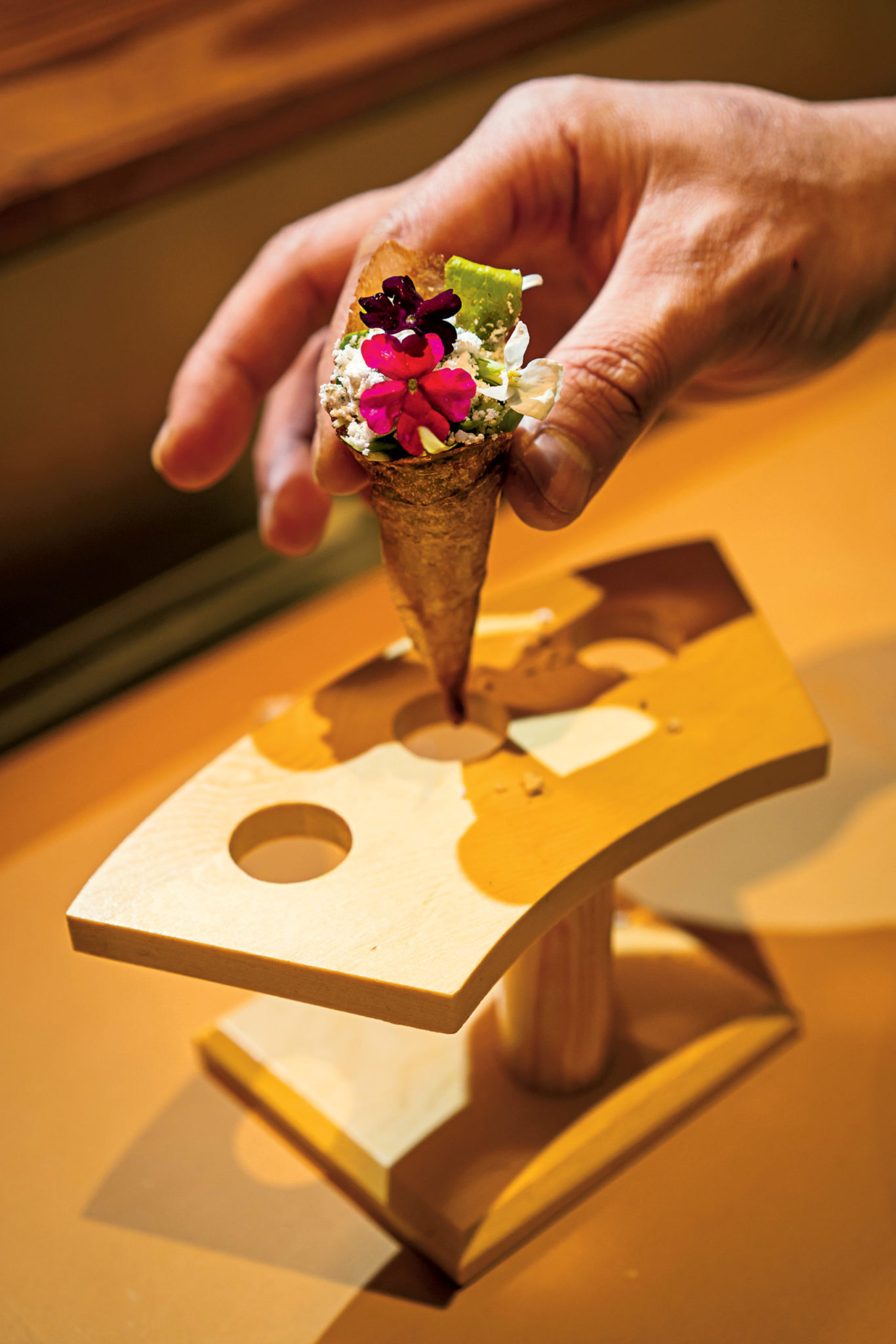 It takes a day to make delicate cones of potato starch, soy, and yuzu, which are used instead of nori for hand rolls stuffed with baby lettuce, orange powder, and edible flowers. Photograph by Scott Suchman.