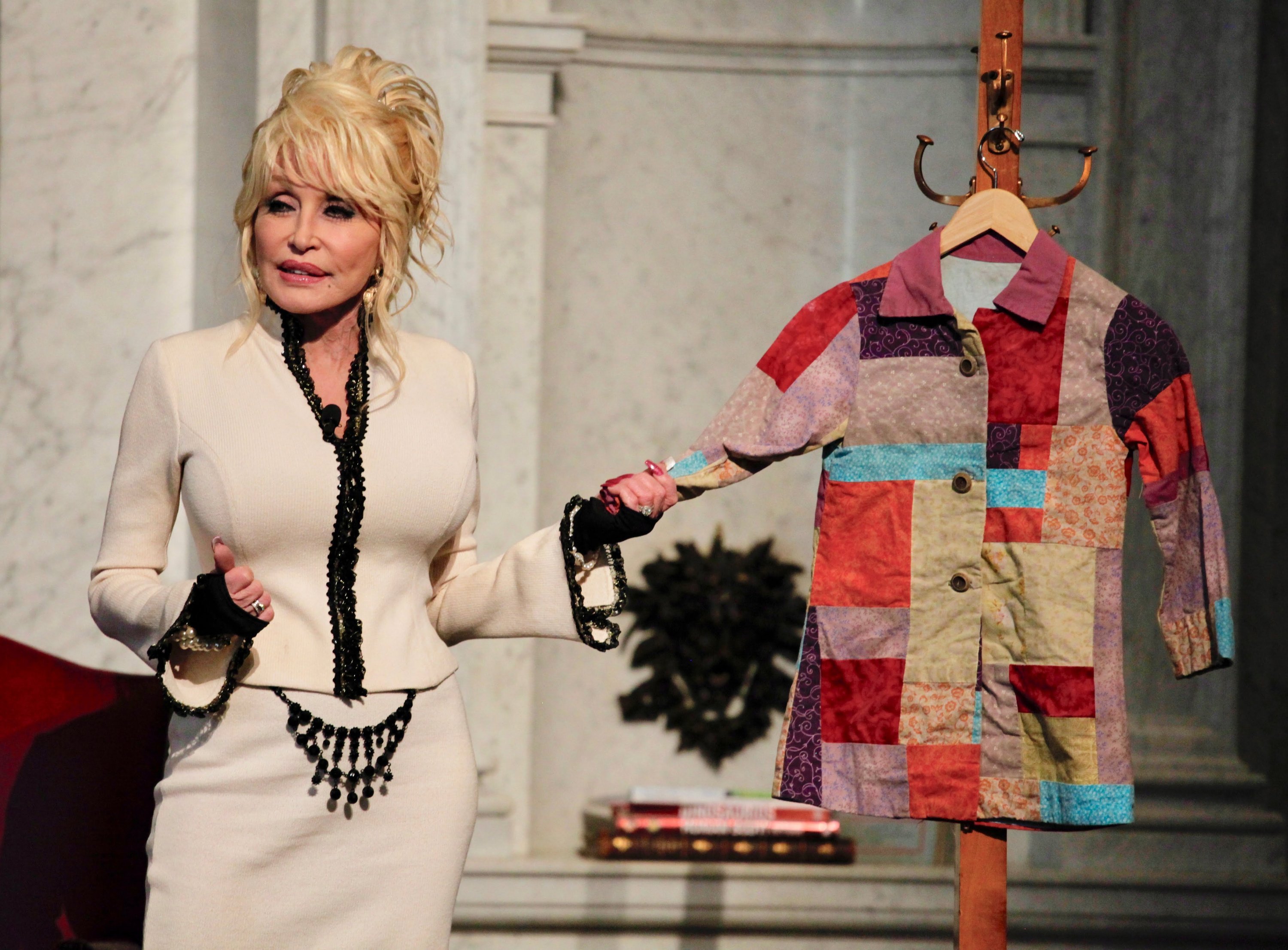 Parton with a replica of the coat that inspired her hit song and book. Both are based on a true story from Parton's childhood: her mother made her a coat out of rags given to the family and taught her to be proud of herself despite growing up in poverty. The book is widely used to discuss and address bullying. 