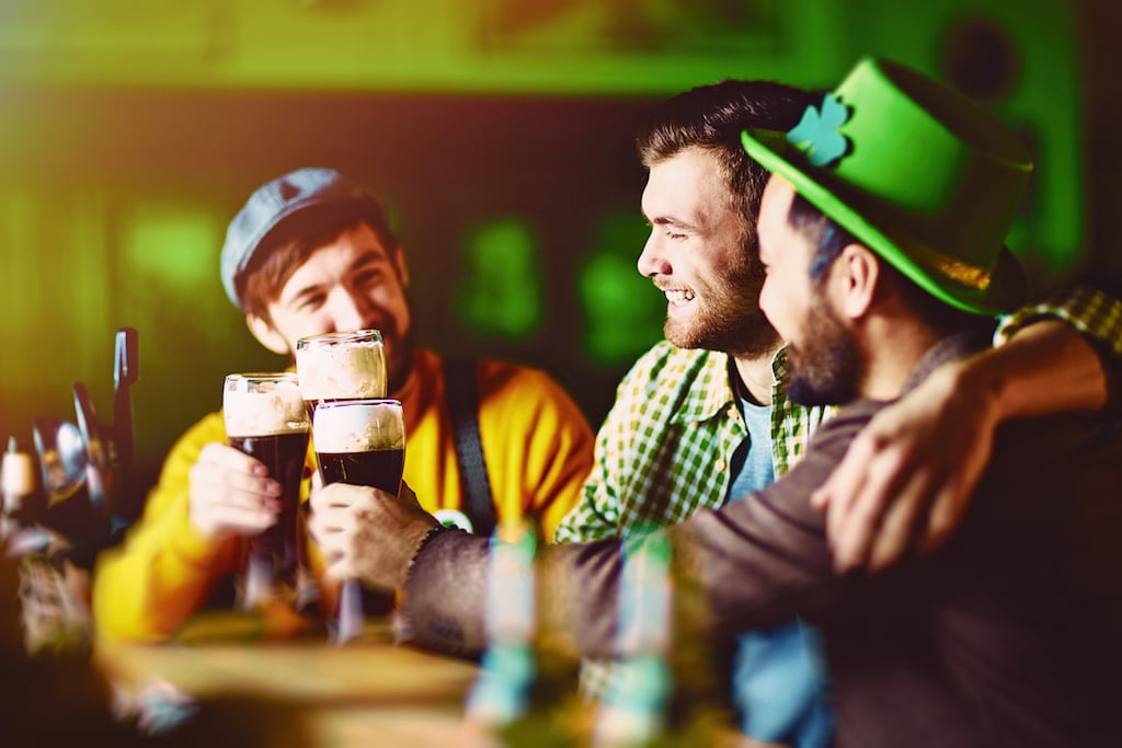 Three slightly drunk friends dressed in traditional green enjoying dark beer during meeting in Irish Pub on St. Patricks day