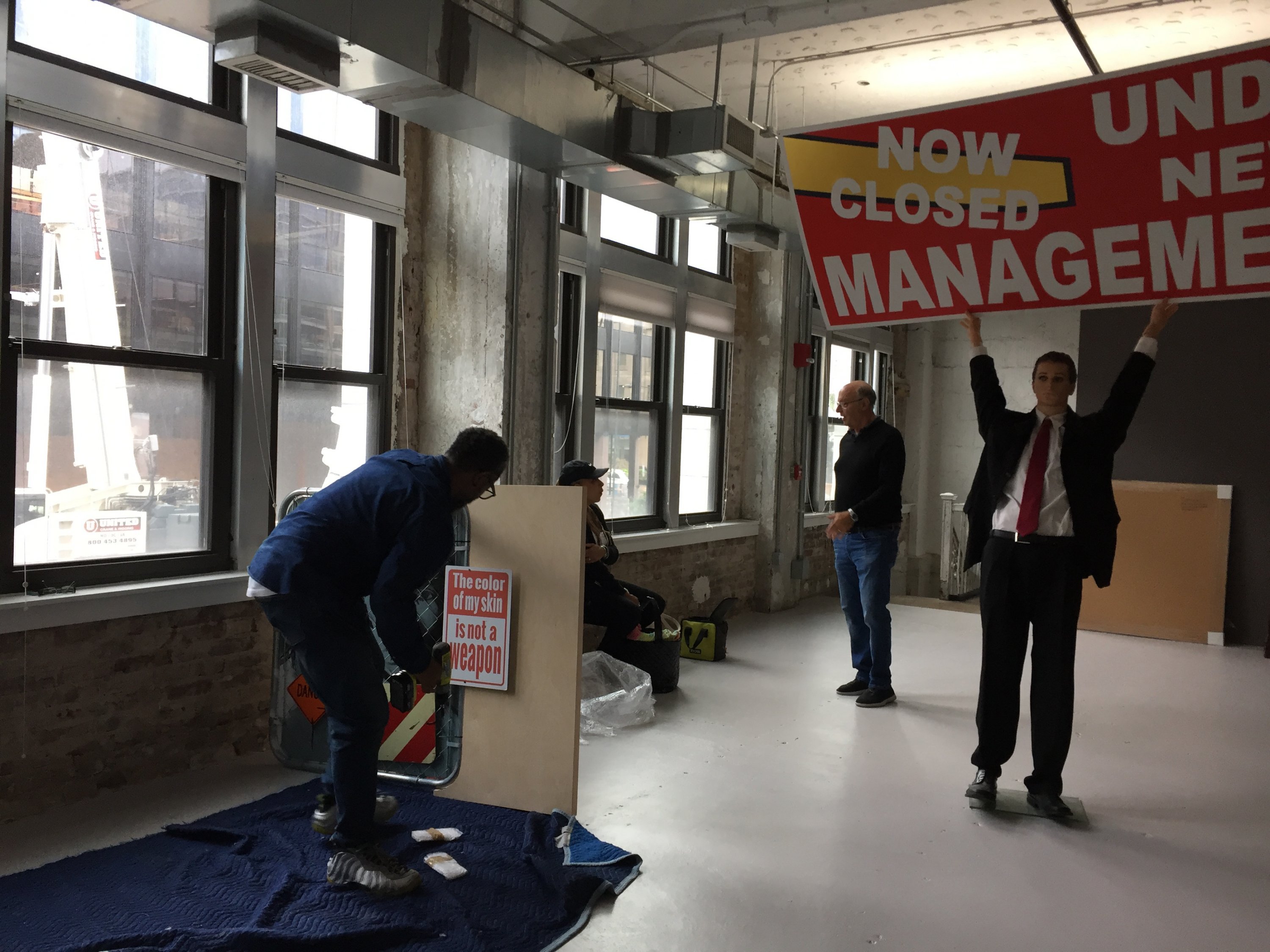 On the left, Jean Icart-Pierre installs his "Street Level" series in the gallery space. The fake man in the middle represents Paul Ryan in TK PIECE by TK ARTIST.