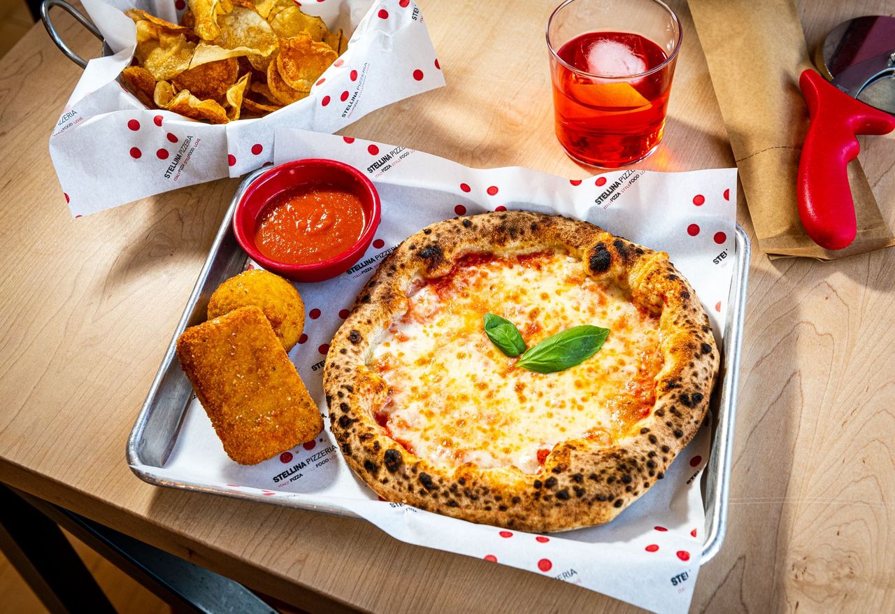 A pizza surrounded by small appetizers and a cocktail