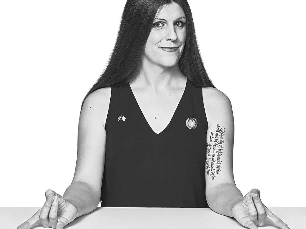 Portrait of Danica Roem with her arms leaning against a table, on both hands making the rock on hand gesture.