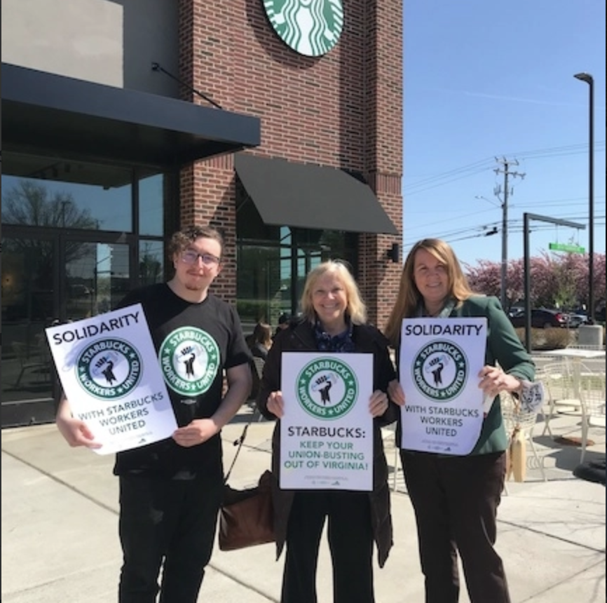 Starbucks barista Declan Galvin outside the Leesburg store with Virginia State Delegate Wendy Gooditis and Virginia State Senator Jennifer Boysko. All three people are holding Starbucks Workers United signs.