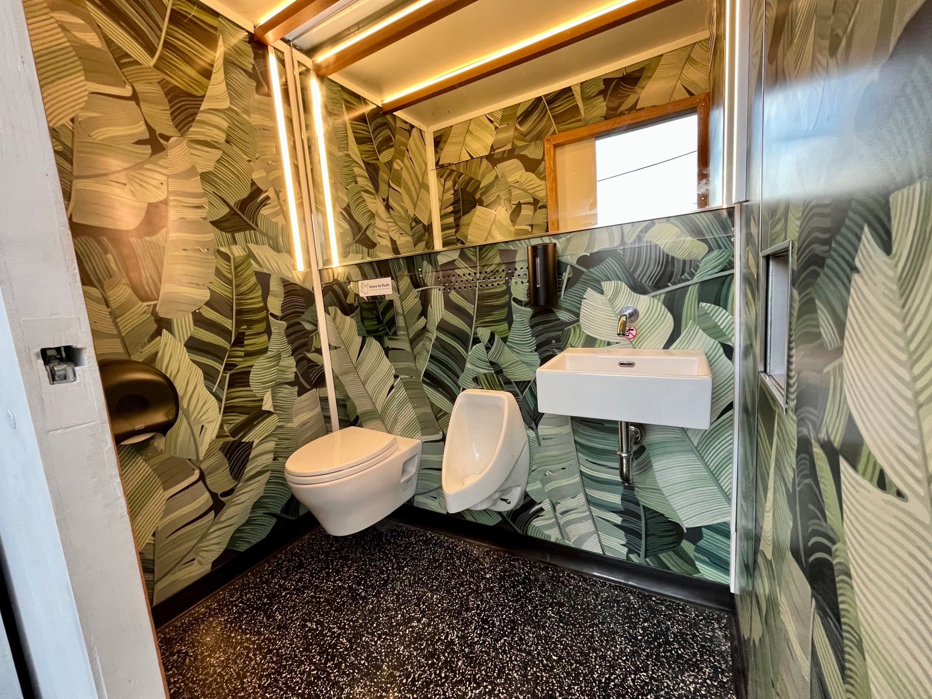 Inside a "Throne," a portable bathroom created by Throne Labs. There's a toilet, urinal, sink, and mirror, and the walls are decorated with a jungle print.