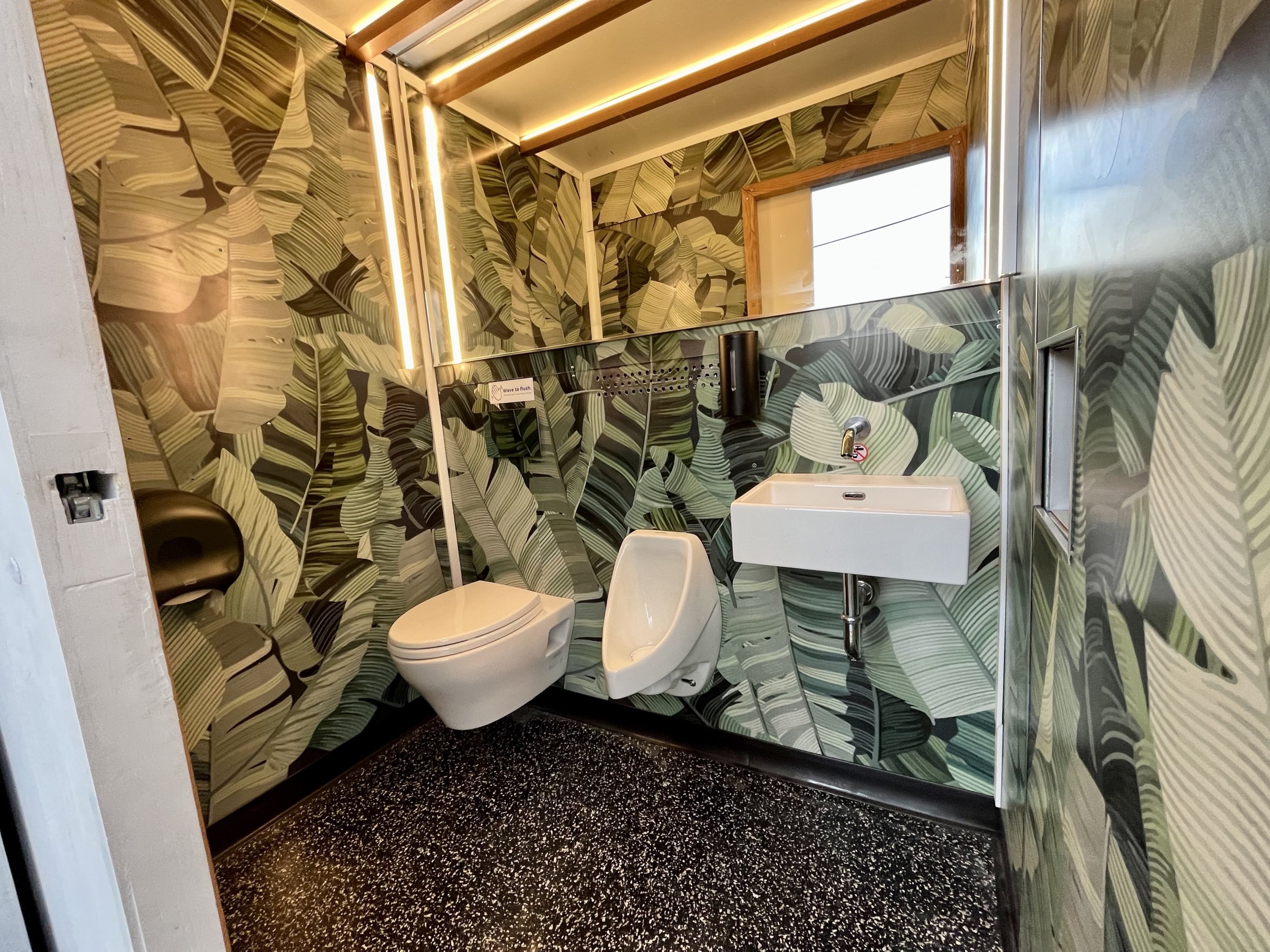 in a "throne" A portable bathroom created by Throne Labs.  There is a toilet, sink, sink and mirror, and the walls are decorated with a forest print.