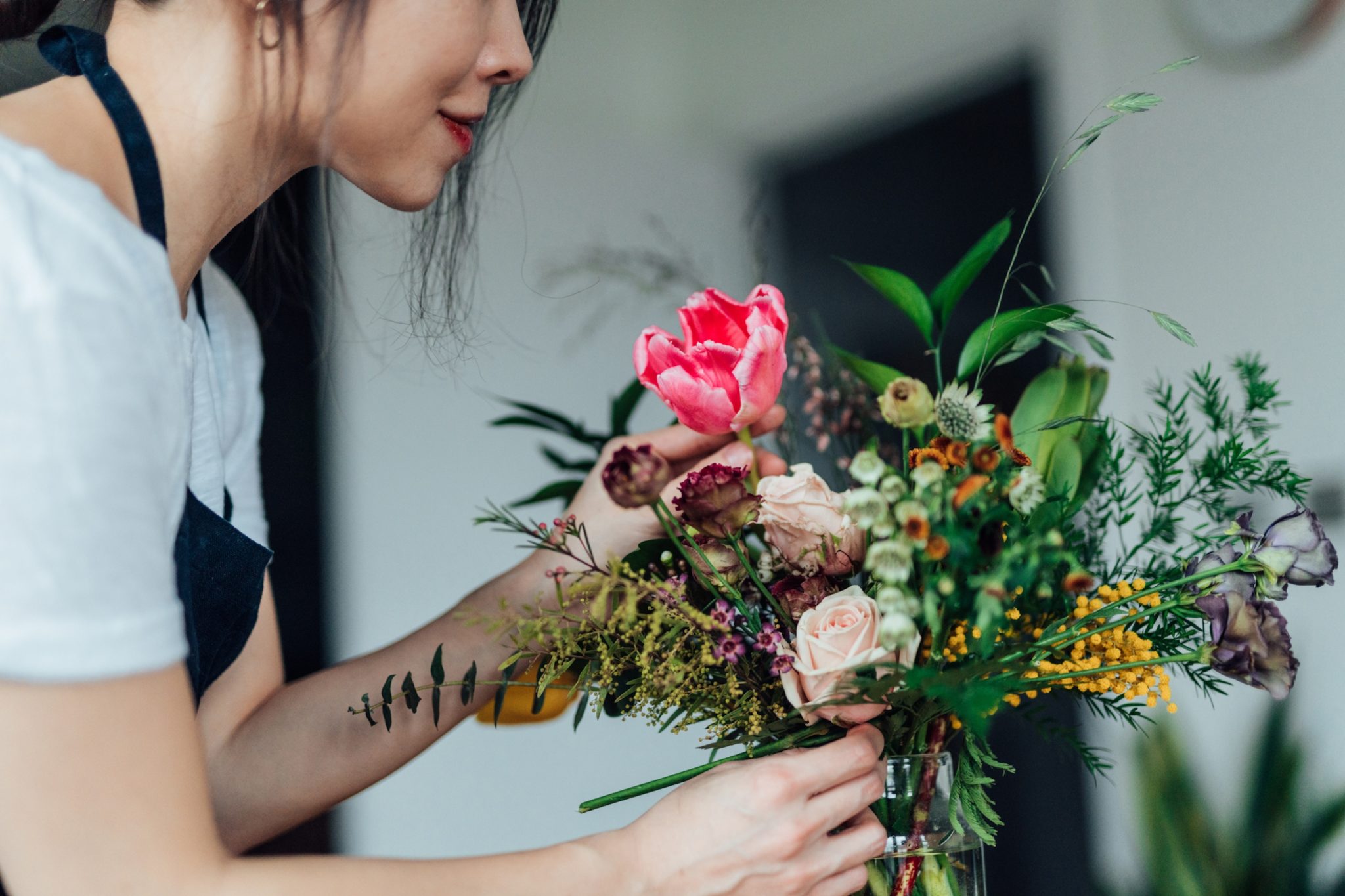 A woman arranging flowers, including a pink tulip.